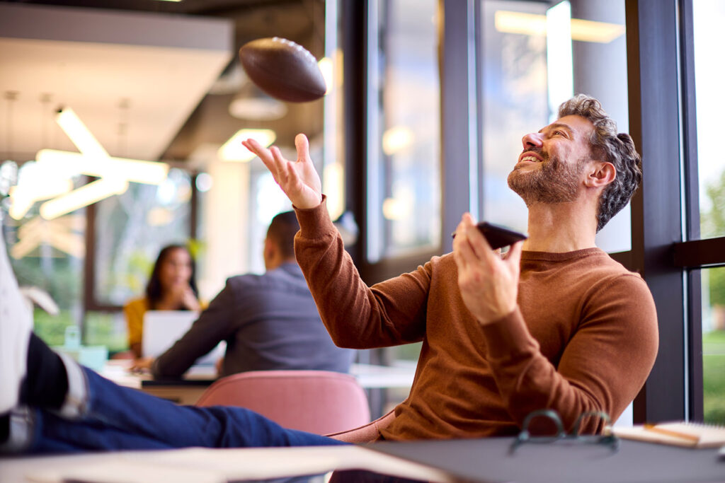 man sitting at desk tossing football in the air